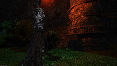 In the dark of night, a younger Sarnai in her traditional attire stands in the rain in front of the entrance to Bardam's Mettle, marked by large stone pillars wrapped with rope. The darkness is pierced by the flaming torch, and she looks behind herself hes