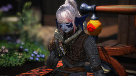 Sarnai, still wearing her gray coat, sits on a bench in her yard. Her eyes are closed and her hand is held to her chest.